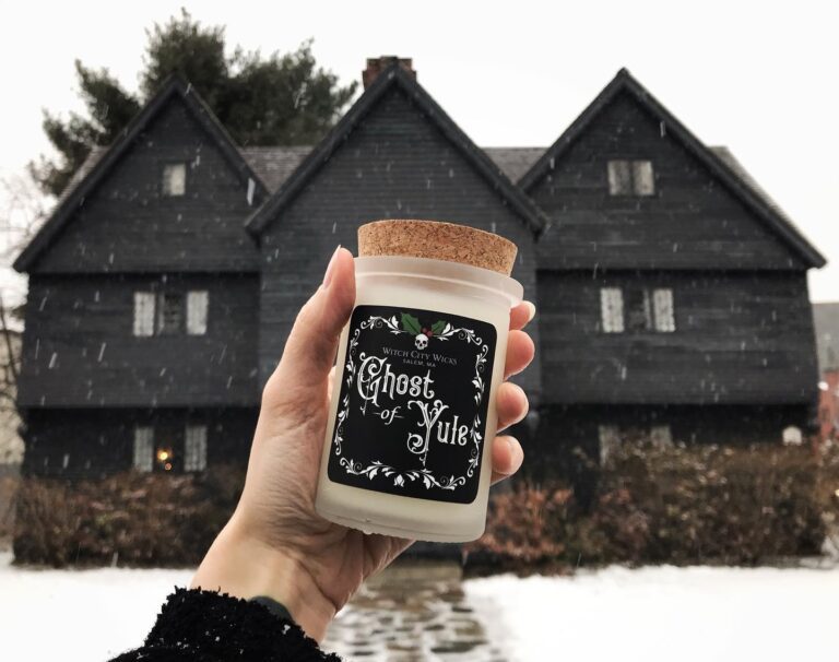 Hand holding a candle in front of the Salem Witch House in the snow