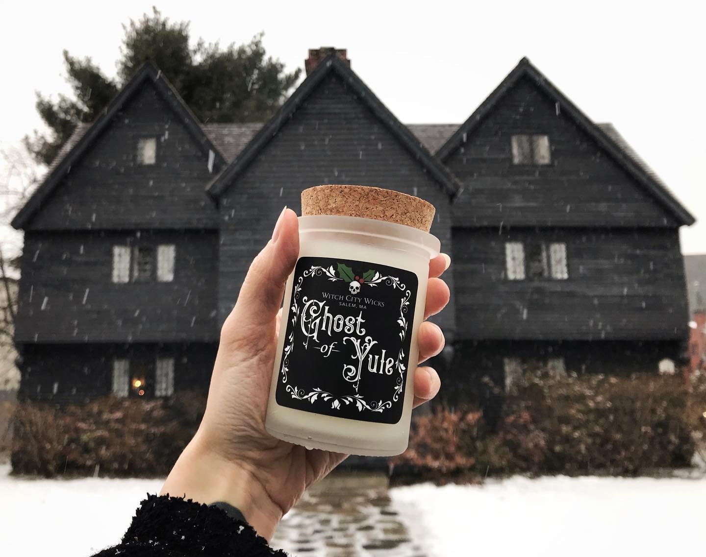 Hand holding a candle in front of the Salem Witch House in the snow