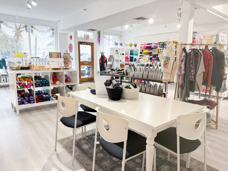 Inside Circle of Stitches on Wharf Street in Salem: shelves of hand-dyed yarn, knitwear, and a white worktable with chairs