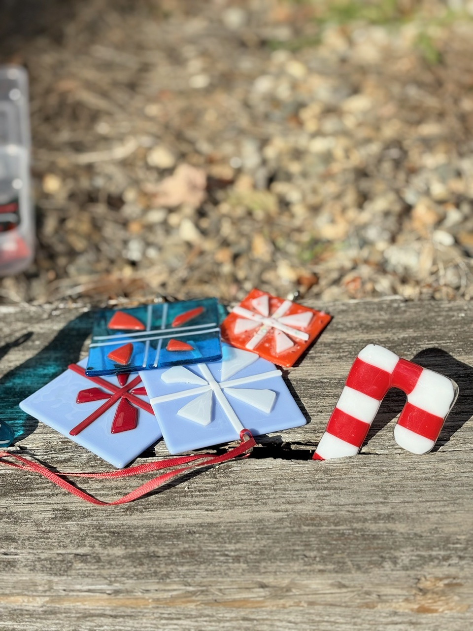 Fused glass ornaments shaped like wrapped presents and a candy cane, made at North Shore Glass School